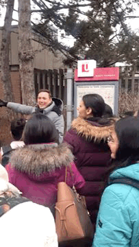 A group of students in a university courtyard standing in front of a sign with the York University logo, with a professor pointing out directions to a campus location.
