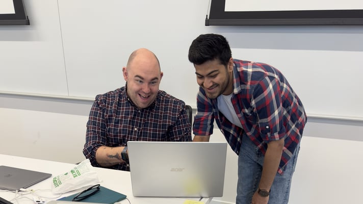 Professor and student looking at the laptop screen and laughing together. the backgroud appears to be a Classroom whiteboard