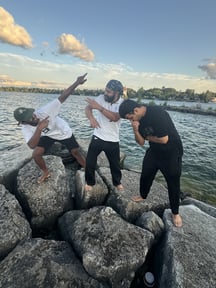 "Tabrej Siddiqui and his friends from York University are having fun and striking playful poses on large rocks by the water. The sky is clear with a few clouds, and the group is enjoying a relaxed moment by the lakeside."