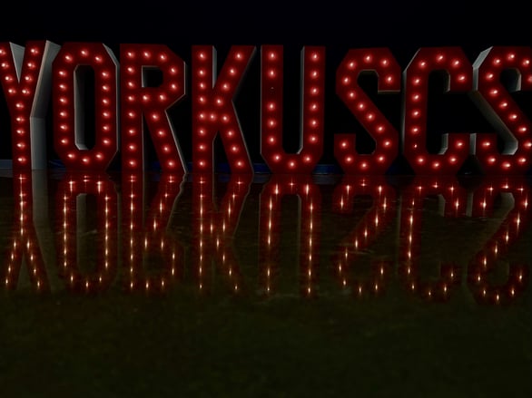 A red neon sign with the words "Yorkscs" written in it. The sign is lit up and reflected in the floor.