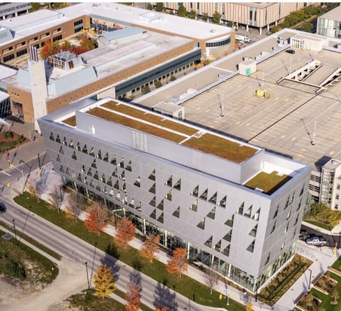 An aerial view of a modern building with a green roof and geometric design on the York University campus, surrounded by other campus buildings and a parking lot.