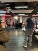 Event in a dimly lighted hall with a bunch of people on the right side of the frame, and a speaker behind the podium on the left side of the frame.