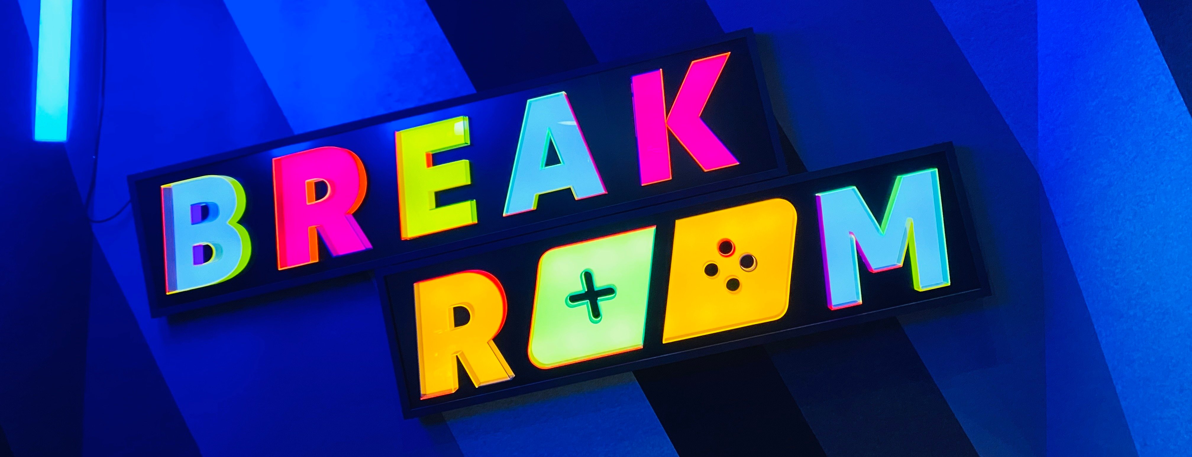 A brightly colored "Break Room" sign with stylized letters and playful icons against a blue background.