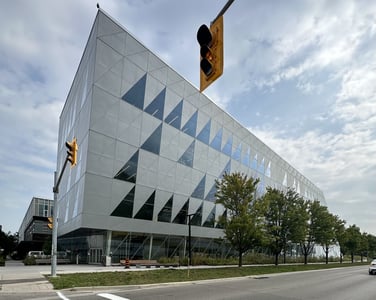 An exterior view of the modern, geometric building of York University's School of Continuing Studies. The building features a unique triangular window design, with traffic lights and trees visible in the foreground.
