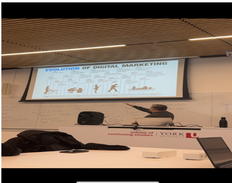 A digital marketing classsroom board where a professor explaining some thing by looking at the board standing near the table.