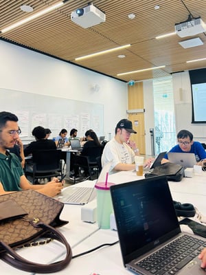 Classroom at York School of Continuing Education with students working on laptops and engaging in discussions, modern lighting and ceiling design, and whiteboards filled with notes in the background.