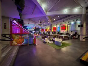 Dim room with arcade games, pool table and chess board with few people using the equipments.