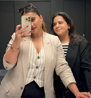 Two girls posing for a mirror selfie. One of them holding a phone in one hand