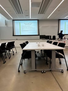 A classroom at York University with a presentation slide on the screen titled "Group Work: Class Participation." The room features modern furnishings, including wheeled tables and chairs. There is a person standing near the front of the room.
