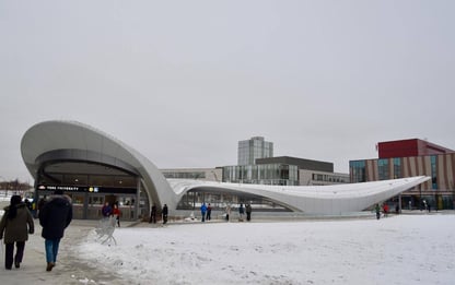 York University's subway station entrance with a modern, curved design on a snowy day. People walk toward the entrance, with campus buildings visible in the background.