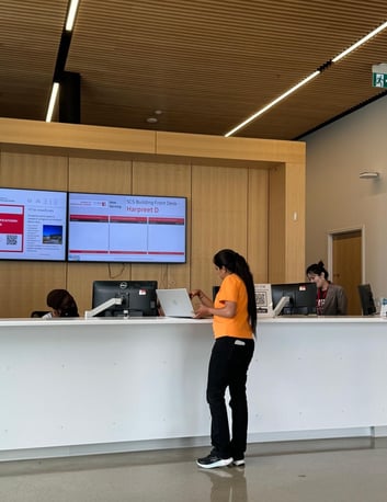 A student connecting with staff at the help desk area in York University, with computerized screens showing information behind the scenes.