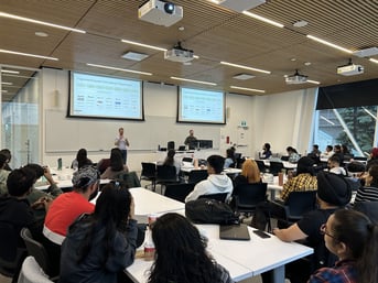 Guest lecturers Ben Wise and Dustin Titus presenting to a classroom of Digital and content marketing students at York University School of Continuing Studies. The lecture focuses on the fragmented ecosystem that makes up 'Programmatic,' with detailed slides displayed on large screens. Students are attentively listening and taking notes in big, well-lit classroom