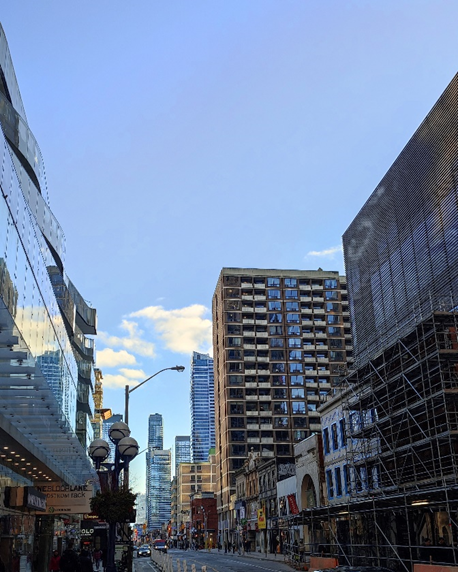 A photo of a street in Toronto Downtown. It’s a bright sunny day with clear sky, there are a lot of glass buildings.