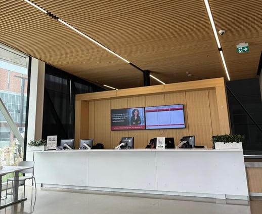 A service desk at York University including a wooden wall, computers, and a screen projecting information above.