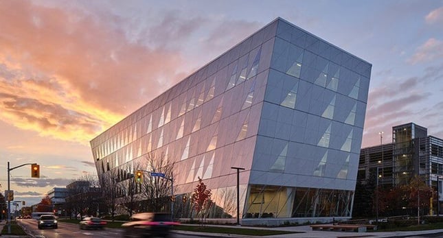 The York University School of Continuing Studies building at sunset, showcasing it's twisted design located right along side the street with traffic lights and cars passing by