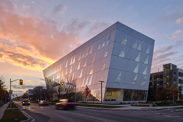 The York University School of Continuous Studies building with cars speeding on the road in front of it. The background features a stunning blue to pink transitional sky.