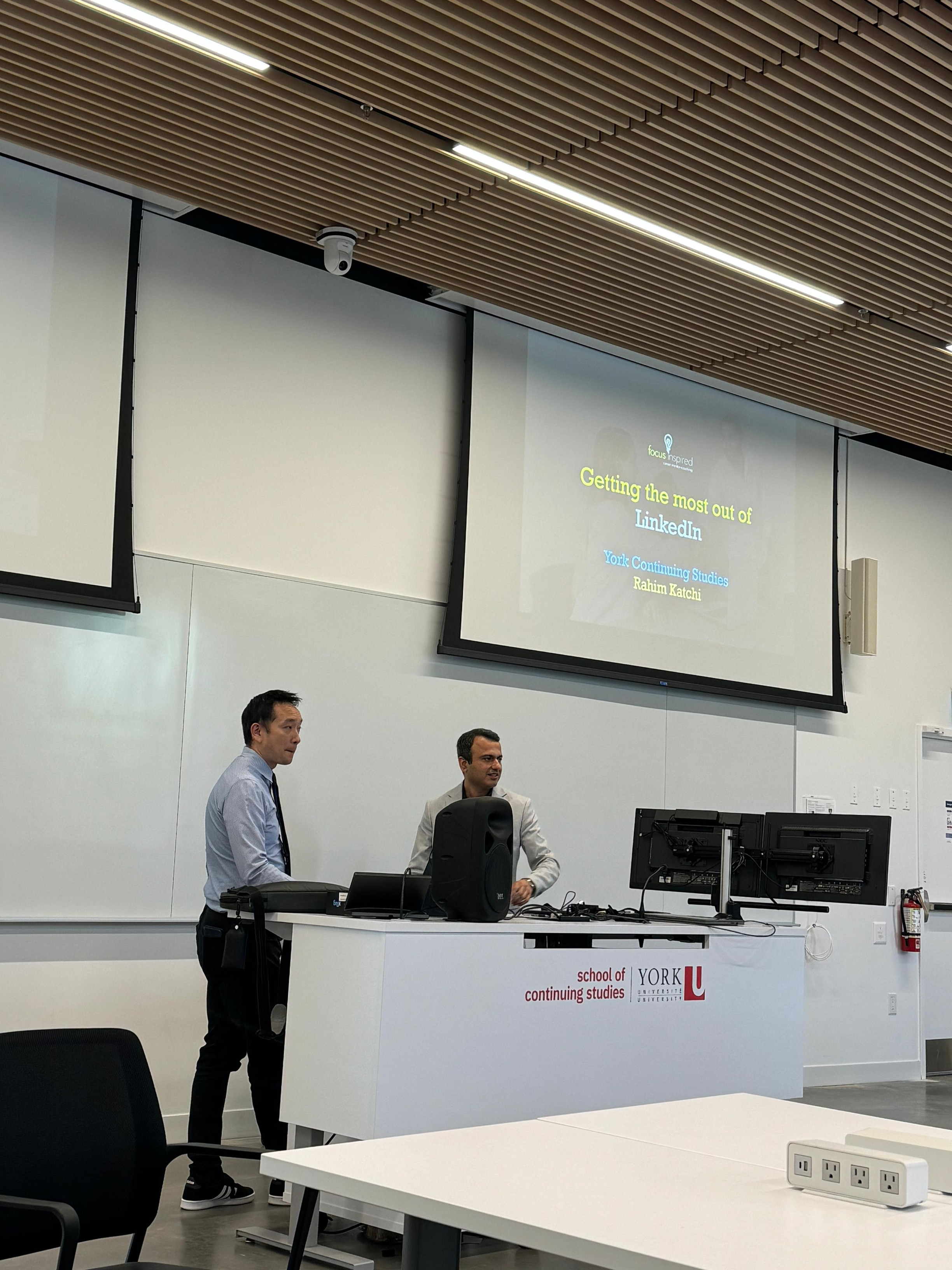 Two men standing in front of a lecture room with a presentation screen displaying 'Getting the most out of LinkedIn' at York University's School of Continuing Studies.