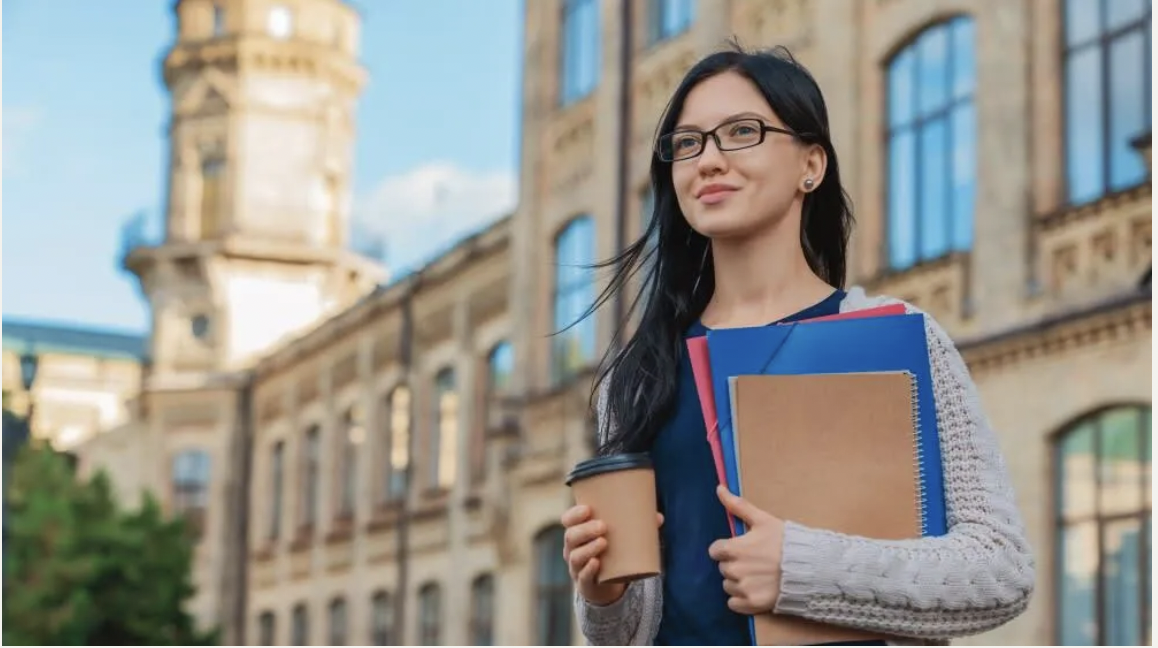 An international student standing with books in front of the university
