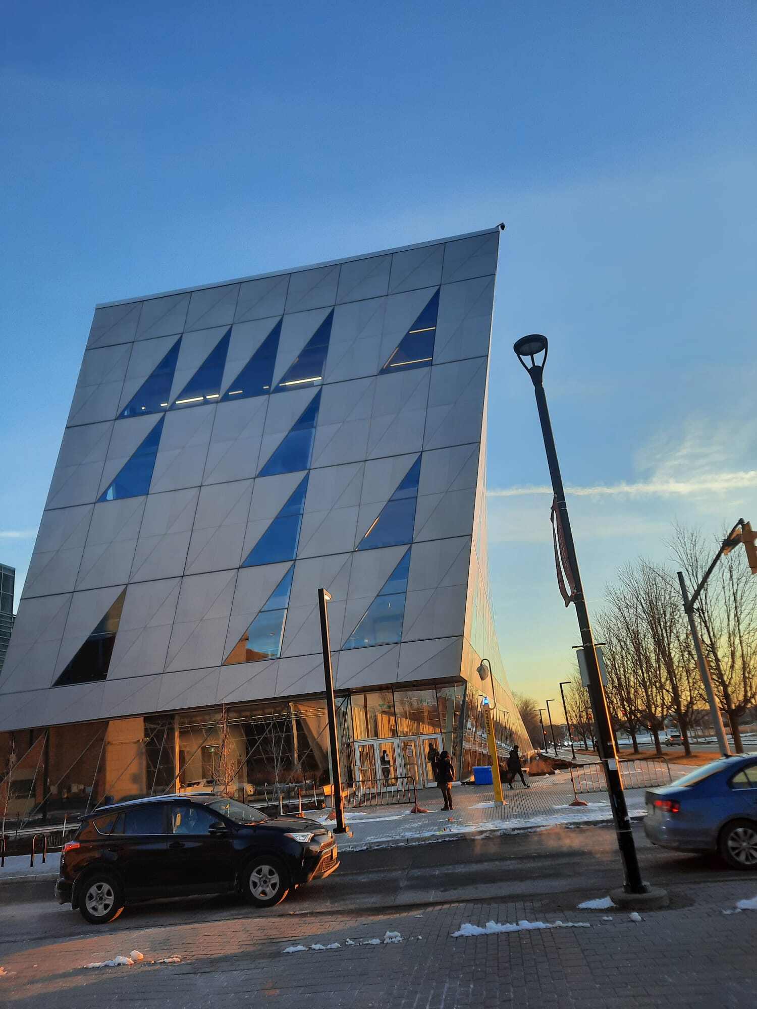 A uniquely designed building with triangular windows, having little snow on the ground and a car parked infront.